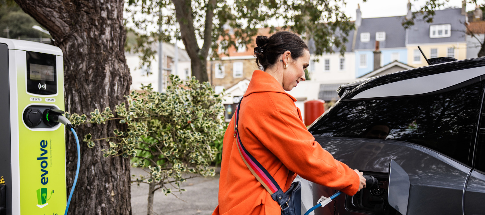 Lady wearing a red coat plugging the charging cable into her electic car